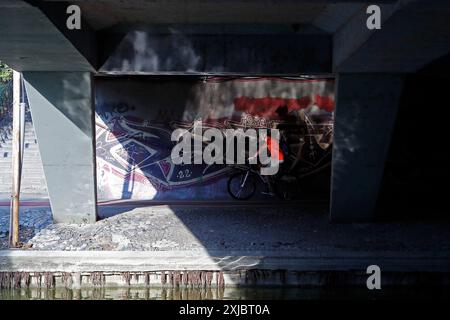 Bucarest, Roumanie. 17 juillet 2024. Un homme monte un vélo sous un pont dans un parc de Bucarest, Roumanie, le 17 juillet 2024. L'Administration météorologique nationale roumaine (ANM) a prolongé ses avertissements de chaleur rouge et orange jusqu'à mercredi, affectant tout le pays dans un climat de canicule en cours. Crédit : Cristian Cristel/Xinhua/Alamy Live News Banque D'Images