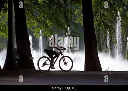 Bucarest, Roumanie. 17 juillet 2024. Un homme fait du vélo près d'une fontaine dans un parc de Bucarest, Roumanie, le 17 juillet 2024. L'Administration météorologique nationale roumaine (ANM) a prolongé ses avertissements de chaleur rouge et orange jusqu'à mercredi, affectant tout le pays dans un climat de canicule en cours. Crédit : Cristian Cristel/Xinhua/Alamy Live News Banque D'Images