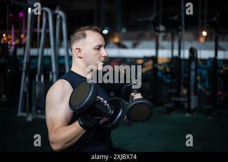 Un homme soulève des poids tout en s'entraînant dans une salle de gym faiblement éclairée. Banque D'Images