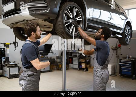 Mécaniciens automobiles travaillant sur l'entretien des véhicules dans un garage moderne Banque D'Images