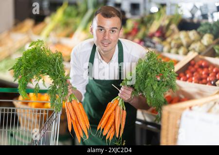 Le propriétaire du magasin dispose des bouquets de carottes biologiques sur l'étalage Banque D'Images