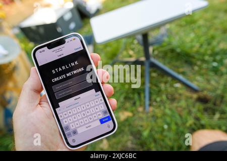 Allemagne - 21 avril 2024 : une personne tient un smartphone montrant l'écran de l'application Starlink pour créer un réseau, avec la configuration de l'antenne Starlink Gen 3 de SpaceX visible en arrière-plan sur une surface herbeuse Banque D'Images