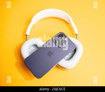 Paris, France - Jun 11, 2023:un iPhone Apple avec une configuration triple caméra repose sur un casque blanc sur un fond jaune vif, mettant en valeur un design moderne et minimaliste Banque D'Images