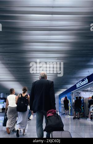Palma, Espagne - 11 juillet 2024 : vue arrière de voyageurs marchant à travers un terminal d'aéroport, avec un magasin WHSmith visible sur le côté et un homme tirant une valise, soulignant l'environnement occupé de l'aéroport Banque D'Images