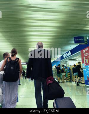 Palma, Espagne - 11 juillet 2024 : voyageurs marchant dans un terminal d'aéroport avec un magasin WHSmith sur la droite, avec un homme tirant une valise dans un environnement animé. Banque D'Images