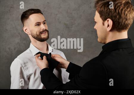 Deux hommes, vêtus d'élégants costumes, se tiennent proches l'un de l'autre. Un homme est en train de réparer le noeud papillon de l'autre. Banque D'Images