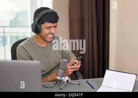 Jeune homme engrossé dans le téléphone tout en enregistrant dans le home studio. Parfait pour les podcasts, la création de contenu audio et le style de vie technologique. Banque D'Images