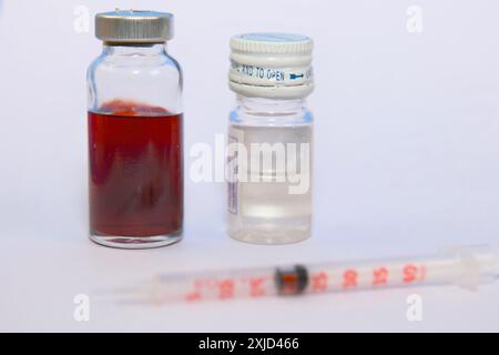 Deux flacons en verre contenant des liquides clairs et colorés avec une seringue en plastique pour mesurer ou injecter des liquides sur fond blanc. Banque D'Images