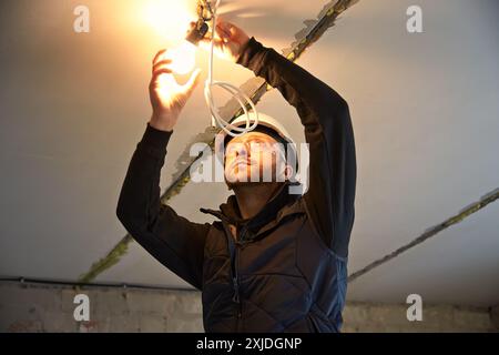 Ouvrier de construction masculin installant une ampoule temporaire au plafond. Banque D'Images