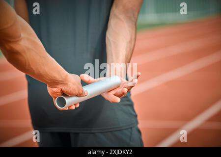 Bâton, fitness et athlètes sur la piste pour la course dans le stade pour courir relais marathon en compétition. Les mains, le sprint et les gens qui passent bâton pour l'équipe Banque D'Images