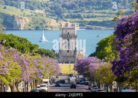 Tour de Belem, Jacaranda Blooming Purple Blue Trees et bateau à voile le jour ensoleillé. Lisbonne, Portugal. Banque D'Images