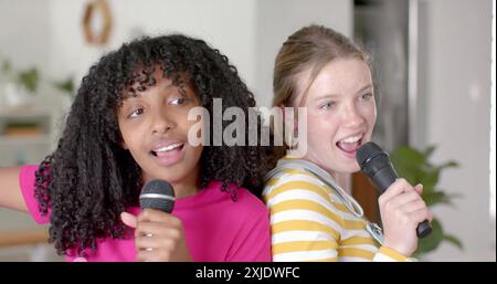 Image de lumières blanches sur des adolescentes heureuses diverses avec des microphones chantant karaoké à la maison Banque D'Images