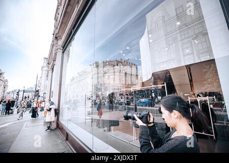 Londres, Royaume-Uni - 10 octobre 2023 : Une femme à Londres, Royaume-Uni, se tient sur Regent Street et prend une photo de la façade d'un magasin, capturant le reflet d'un Banque D'Images