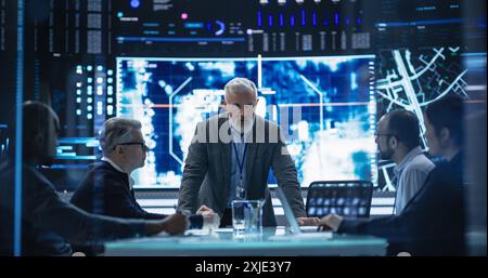 Groupe diversifié d'experts en cybersécurité surveillant une opération active avec la technologie de suivi par satellite. Bureau de surveillance avec des spécialistes multiethniques qui suivent un véhicule cible en terrain urbain Banque D'Images