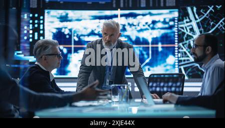 Groupe diversifié d'experts en cybersécurité surveillant une opération active avec la technologie de suivi par satellite. Bureau de surveillance avec des spécialistes multiethniques qui suivent un véhicule cible en terrain urbain Banque D'Images