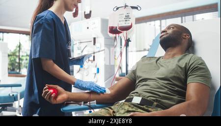 Infirmière caucasienne recevant un don de sang de la troupe de l'Armée noire à l'hôpital militaire. Homme africain pressant la balle en forme de coeur pour pomper le sang dans le sac. Soldat faisant don à des camarades blessés. Banque D'Images