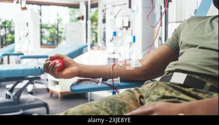 Gros plan de Hand of Black Army Soldier avec cathéter attaché à l'hôpital militaire. Brave African Male Troop Sqeezing Red Ball pour pomper le sang à travers la tubulure dans le sac. Homme faisant don à des camarades blessés. Banque D'Images