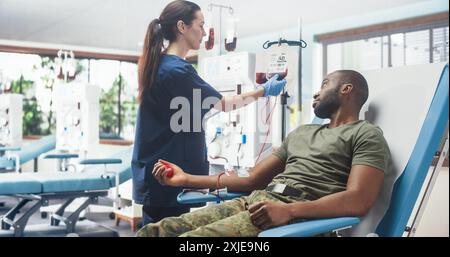 Infirmière caucasienne recevant un don de sang de la troupe de l'Armée noire à l'hôpital militaire. Homme afro-américain pressant la balle en forme de coeur pour pomper le sang dans le sac. Soldat faisant don à des camarades blessés. Banque D'Images