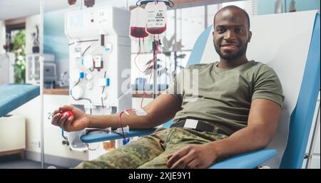 Un soldat de l'armée mâle noir donne du sang pour des camarades blessés à l'hôpital militaire. Brave troupe africaine pressant la balle rouge pour pomper le sang regardant la caméra et souriant. Don pour les hommes en service. Banque D'Images