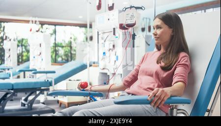 Femme caucasienne donnant du sang pour les personnes dans le besoin à l'hôpital Bright. Donneur femelle pressant la boule rouge en forme de coeur pour pomper le sang à travers la tubulure dans le sac. Don pour les victimes d'accidents. Banque D'Images