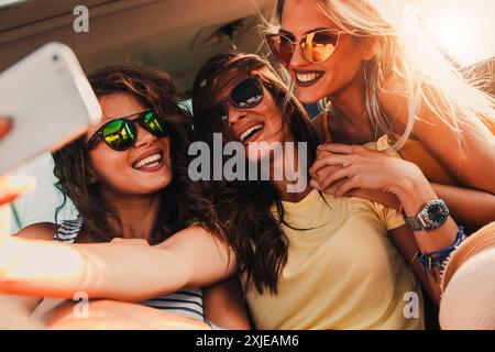 Trois amis féminins bénéficiant dans la voiture. Assis dans le siège arrière et et faire. selfies Banque D'Images