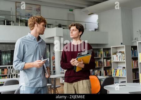 Deux jeunes hommes s'engagent dans une discussion profonde au milieu des livres dans une bibliothèque. Banque D'Images