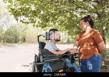 Homme, un utilisateur de fauteuil roulant électrique dans l'étreinte chaleureuse de sa femme, un couple appréciant et montrant leur affection. Handicap et concept d'amour. Banque D'Images