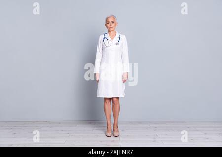 Photo pleine longueur de charmante dame senior médecin thérapeute spécialiste qualifié porter une robe blanche isolée sur fond de couleur grise Banque D'Images
