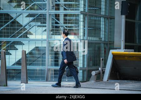 Hong Kong, Chine - 03 janvier 2024 : Un homme en costume et masque passe devant un bâtiment moderne dans le centre de Hong Kong. Banque D'Images