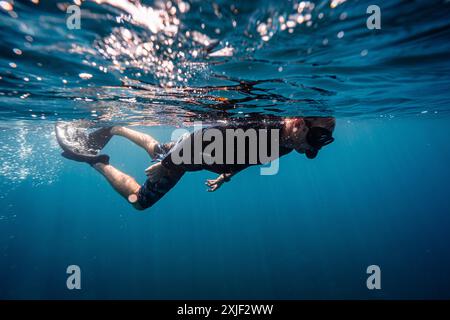 Caucasien homme snorkeler nageant dans les eaux bleues profondes avec masque, tuba, palmes et équipement de natation de garde d'éruption noire Banque D'Images