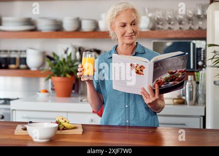 Femme mature, jus et livre de recettes pour l'alimentation, les ingrédients et lire pour les instructions dans la cuisine. Vegan, boisson à l'orange et cuisine pour la nourriture à la maison Banque D'Images
