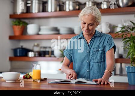 Femme mature, lire et livre de recettes pour le régime, les ingrédients et lire pour les instructions dans la cuisine. Vegan, orange et cuisine pour la nourriture à la maison, femelle Banque D'Images