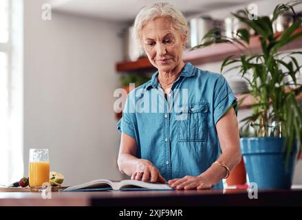 Femme mature, lire et livre de recettes pour le repas, les ingrédients et apprendre pour les instructions dans la cuisine. Vegan, orange et cuisine pour la nourriture à la maison, femelle Banque D'Images