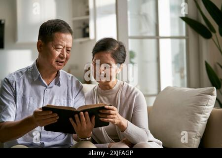 heureux couple asiatique senior assis sur le canapé de la famille à la maison lisant la bible ensemble Banque D'Images