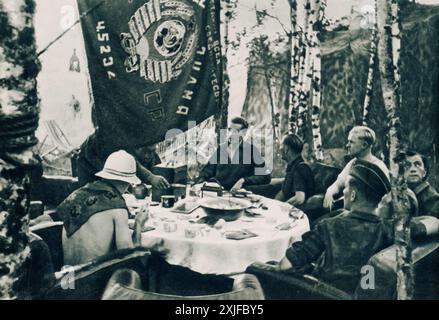 Une photographie montre des soldats allemands rassemblés autour d'une table dans la forêt, assis dans des chaises confortables et non traditionnelles. Prise lors de l'opération Barbarossa en 1941, cette image capture un moment de camaraderie et de répit au milieu de la campagne contre les forces soviétiques sur le front de l'est pendant la seconde Guerre mondiale. Banque D'Images