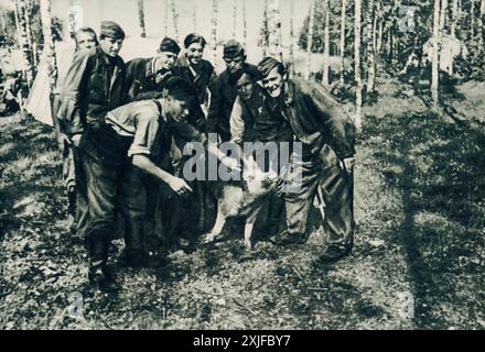 Une photographie montre des soldats allemands rassemblés autour de la mascotte de leur unité, un cochon, posant pour la caméra. Prise lors de l’opération Barbarossa en 1941, cette image offre un aperçu des moments légers partagés par les troupes alors qu’elles avançaient contre les forces soviétiques sur le front de l’est pendant la seconde Guerre mondiale. Banque D'Images