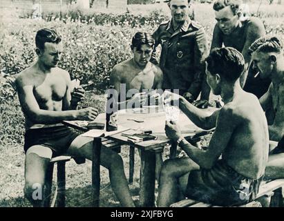 Une photographie en couleur capture des soldats allemands assis autour d'un banc, jouant à un jeu de cartes appelé skat, pendant un bref moment de temps d'arrêt. Prise en 1941 lors de l'opération Barbarossa, elle montre l'occupation allemande de la terre soviétique, alors qu'ils avancent sur le front de l'est. Banque D'Images