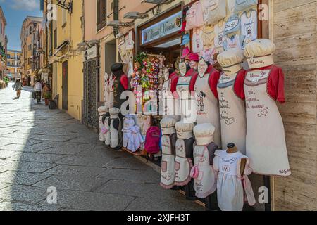 ALGHERO, ITALIE - 4 JUILLET 2024 : rue pittoresque médiévale, typique sarde, avec de petites boutiques de souvenirs traditionnelles. Modèle local de costume de cuisinier exposé Banque D'Images