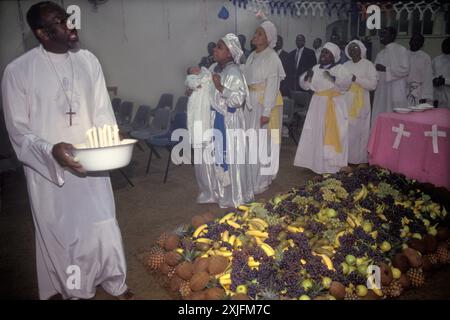 Baptême - une cérémonie de baptême de bébé, les membres de l'église dansent autour de l'énorme pile de fruits. Un pasteur mène la danse, il tient un bol contenant des bougies allumées. Derrière lui une prophétesse, qui est en esprit tenant l'enfant pendant que les femmes dansent dans la célébration d'une nouvelle vie. La prophétesse chante, parlant en langues qui est l'un des dons surnaturels de l'esprit Saint mentionné dans 1 Corinthiens 12:4-10 : Elephant and Castle, Londres, Angleterre, 1993 1990s UK HOMER SYKES Banque D'Images