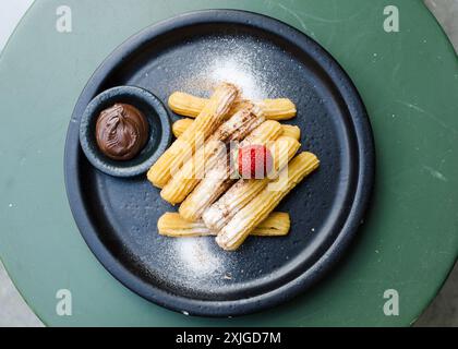 Vue de dessus de délicieux churros dans une assiette noire avec confiture de chocolat et fraise sur le dessus. Banque D'Images