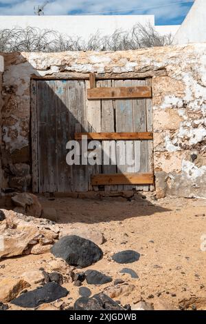 Très vieux bâtiment abandonné avec une porte en bois altérée. Sable dans la rue. Ciel bleu avec des nuages blancs. Caleta del Sebo, la Graciosa, Îles Canaries Banque D'Images