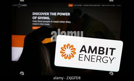 Personne tenant un smartphone avec le logo de la société américaine de marketing multi-niveaux Ambit Energy en face du site Web. Concentrez-vous sur l'affichage du téléphone. Banque D'Images