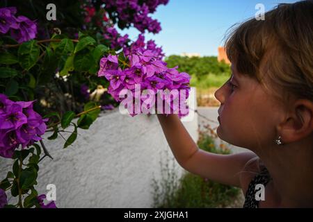 La jeune fille sent les fleurs de bougainvilliers violets avec les yeux fermés. Banque D'Images