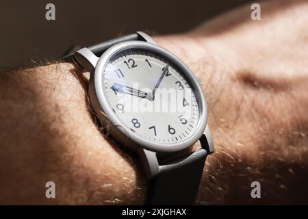 Montre-bracelet mécanique automatique avec cadran d'horloge gris et chiffres arabes noirs dans le boîtier en acier mat sur une main masculine, gros plan photo avec doux sélectif Banque D'Images