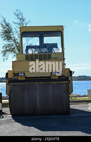 Rouleau à vapeur jaune garé sur une route asphaltée flambant neuve au bord de la mer par une journée ensoleillée. Banque D'Images