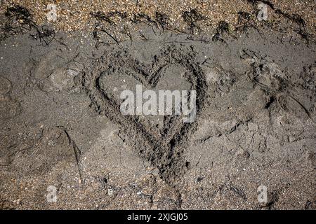 Cœur tiré dans le sable sur une plage emportée par les vagues de l'océan, représentant l'amour perdu. Banque D'Images