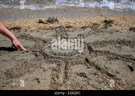 Personne dessine un soleil avec un visage dans le sable sur une plage. Banque D'Images