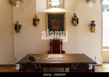 Astorga, Espagne - 4 juin 2023 : un bureau en bois, orné d'un coussin de cuir, est assis devant une chaise majestueuse et richement sculptée avec un coussin en velours rouge. Le Banque D'Images