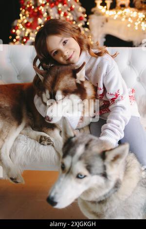 Gros plan de fille mignonne embrassant chien Husky sur fond de noël Banque D'Images