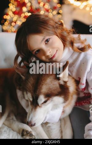 Gros plan de fille mignonne embrassant chien Husky sur fond de noël Banque D'Images